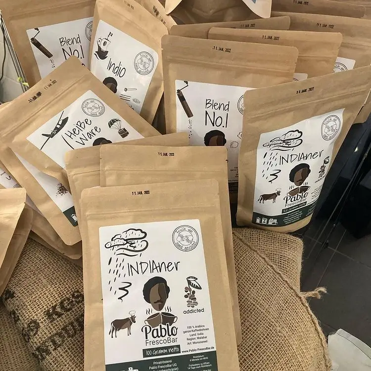 Mehrere braune Kaffeepackungen mit schwarzem Aufdruck in verschiedenen Sorten stehen auf einem Jutesack